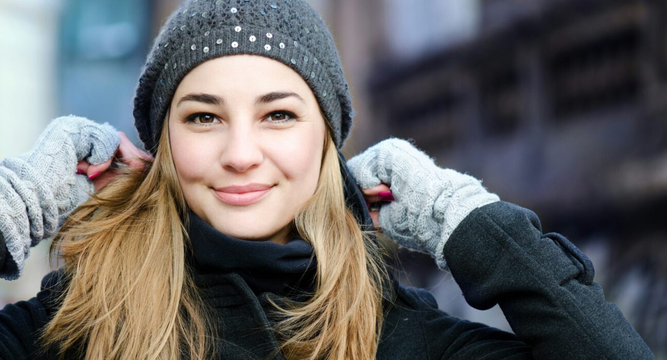 Mujer rubia sonriente con gorro de lana gris y guantes en la calle