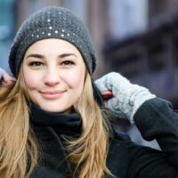 Mujer rubia sonriente con gorro de lana gris y guantes en la calle