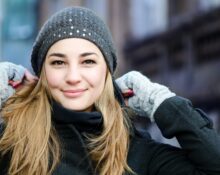 Mujer rubia sonriente con gorro de lana gris y guantes en la calle