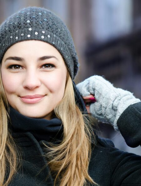 Mujer rubia sonriente con gorro de lana gris y guantes en la calle