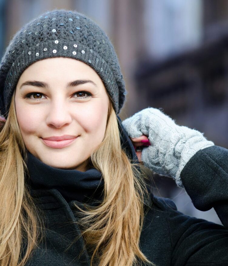 Mujer rubia sonriente con gorro de lana gris y guantes en la calle