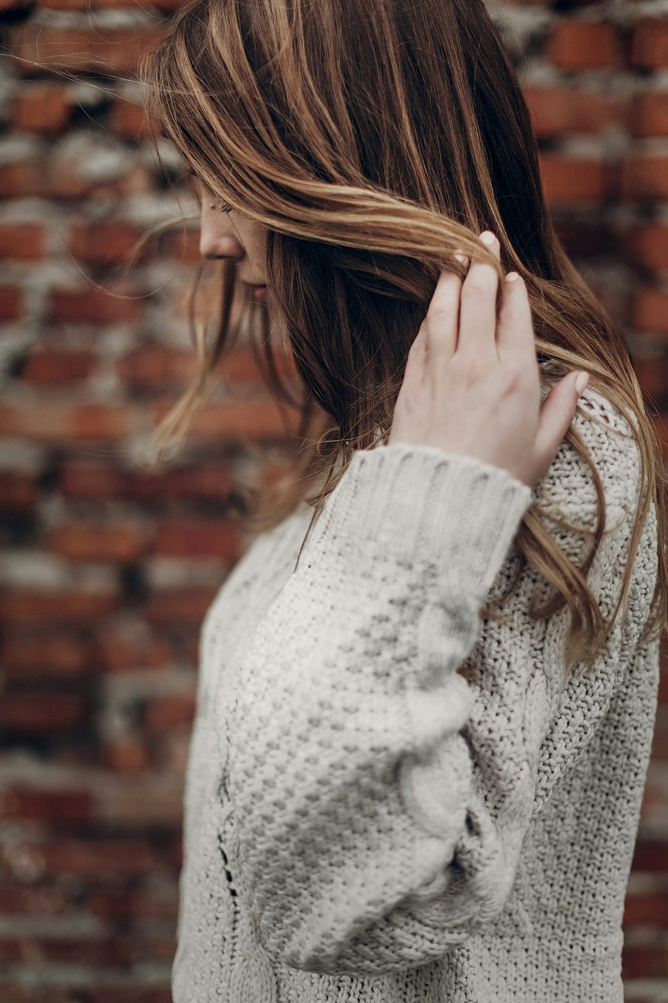 Mujer de melena castaña con reflejos acomodándose el pelo, con suéter de punto