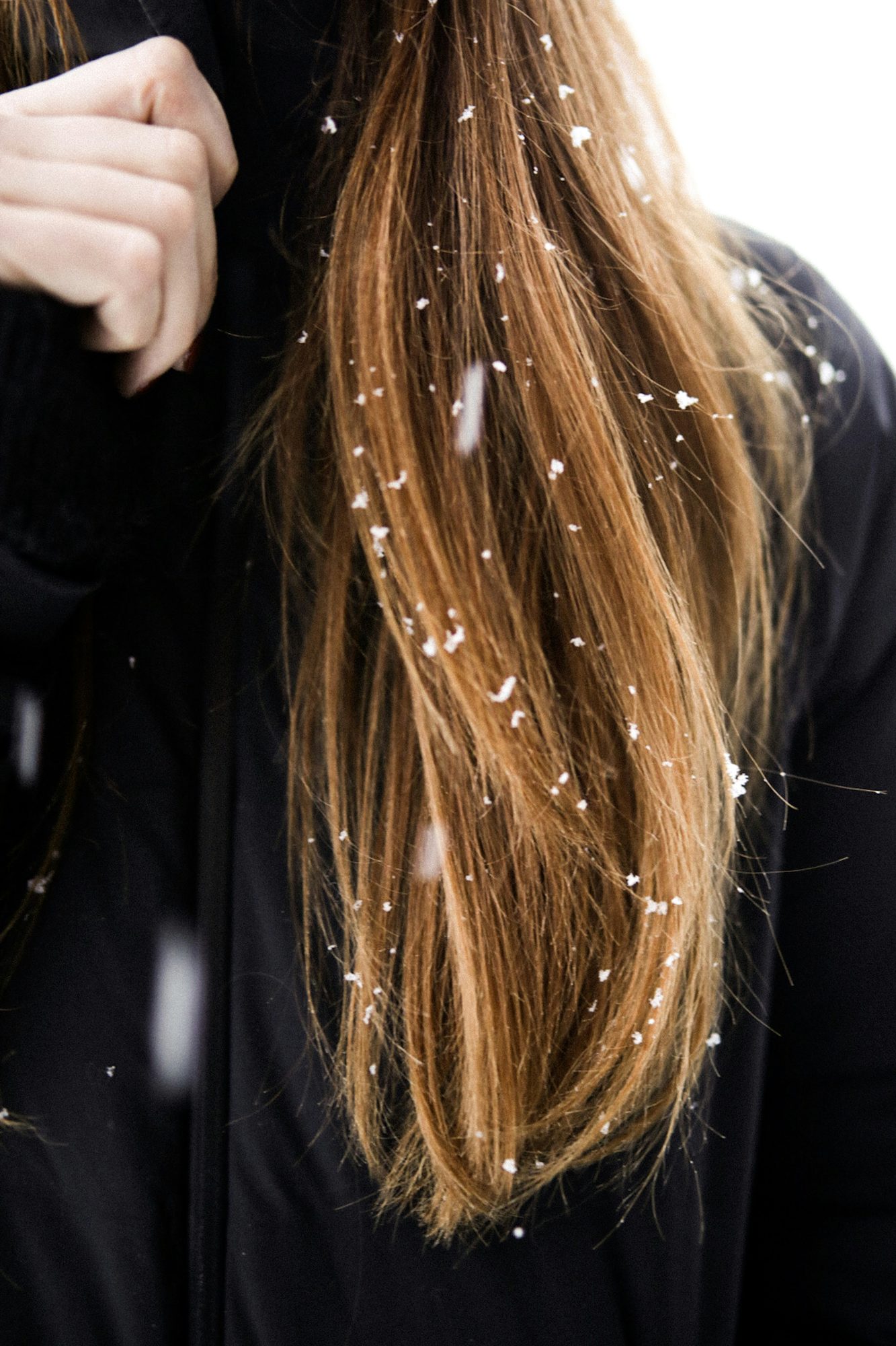 Cabello largo castaño con copos de nieve sobre un abrigo negro