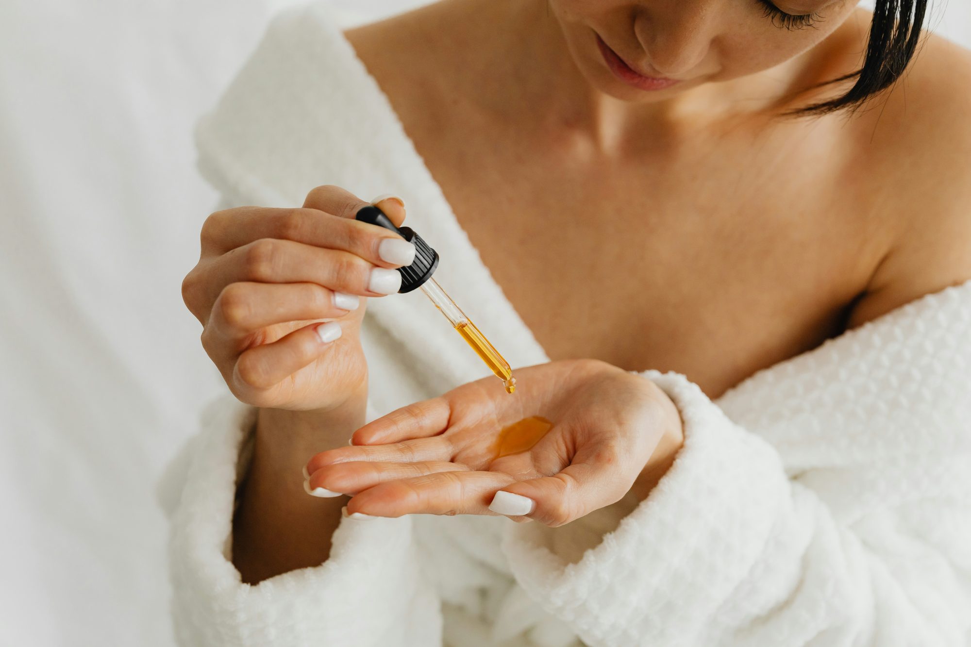 Manos con un gotero dejando caer aceite facial en la palma