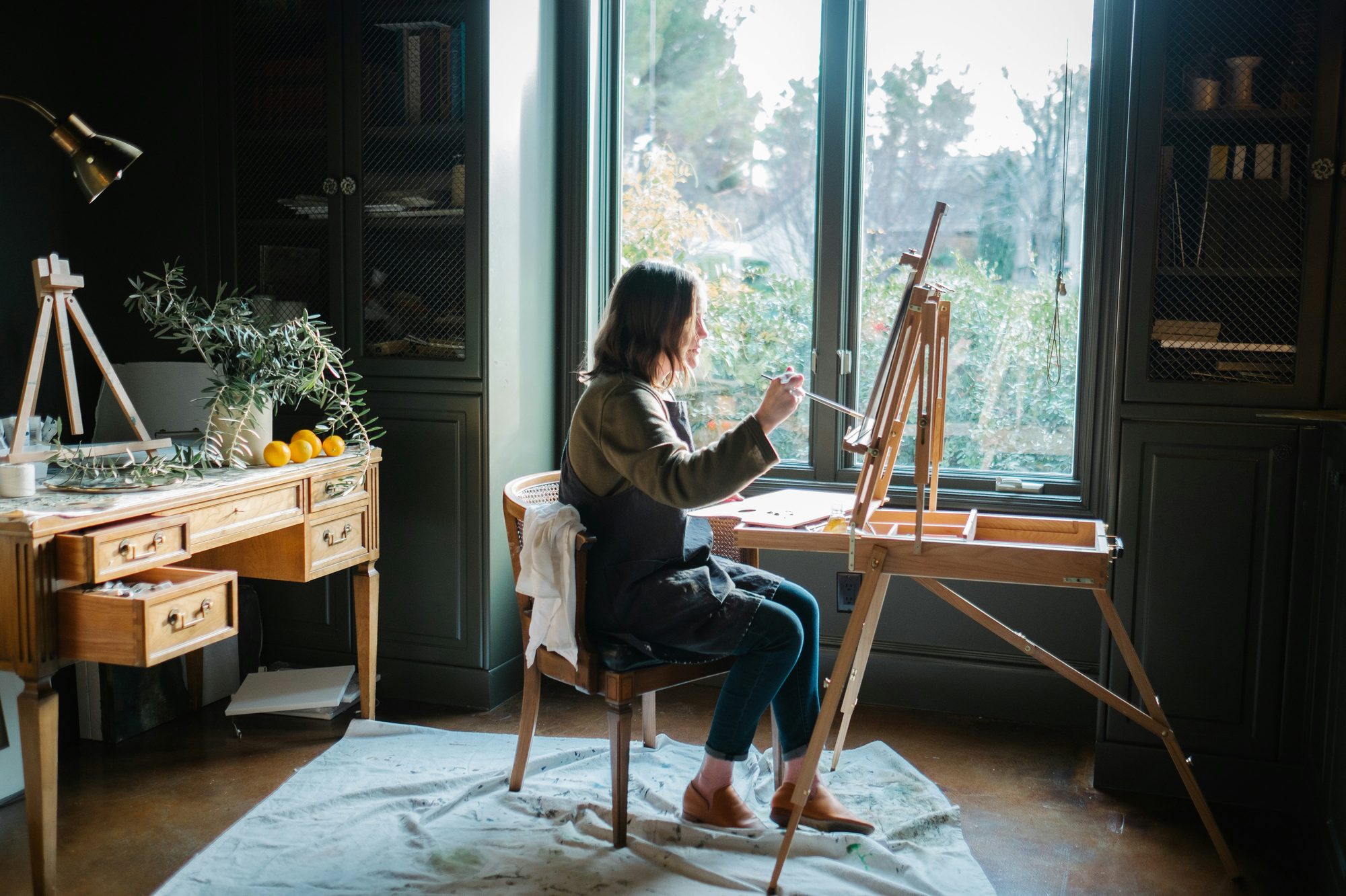 Mujer pintando en un caballete junto a una ventana