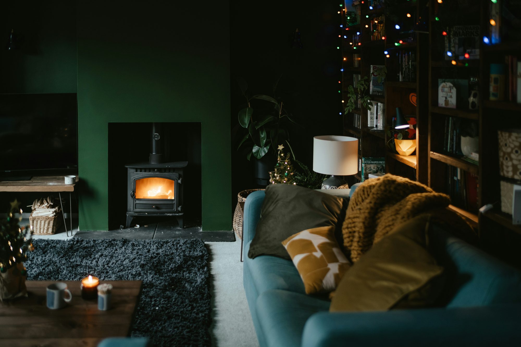 Salón con pared verde, estufa de leña encendida y sofá azul