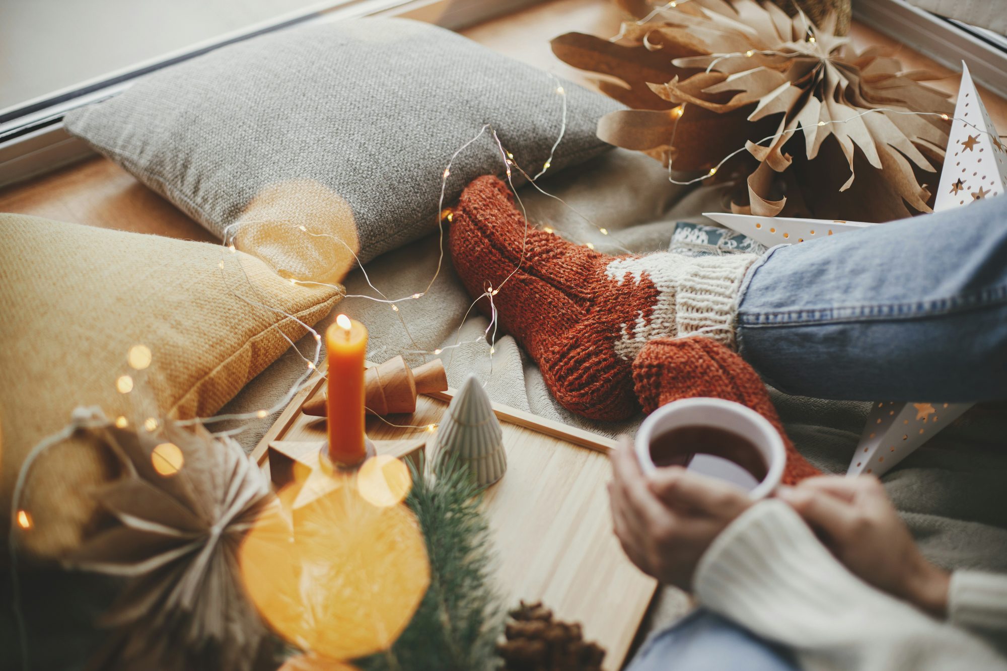 Pies con calcetines de lana junto a velas y una taza caliente
