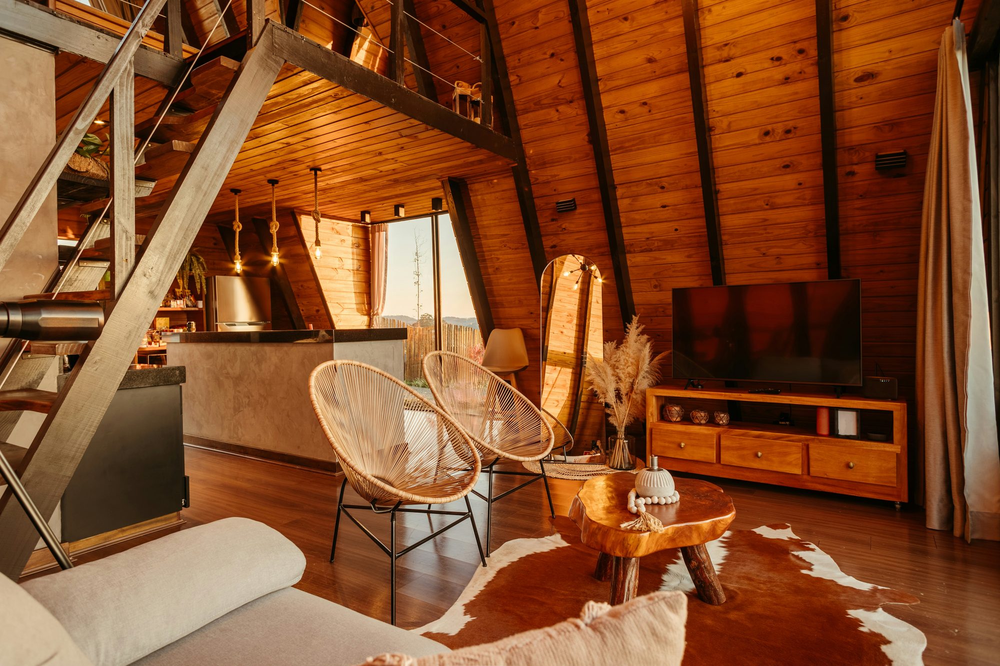 Interior de cabaña de madera con techo inclinado, butacas y alfombra