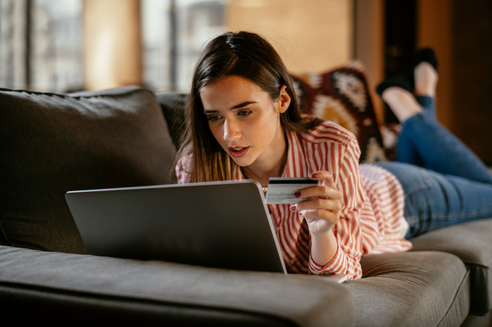 Mujer recostada en el sofá con una laptop y una tarjeta en la mano
