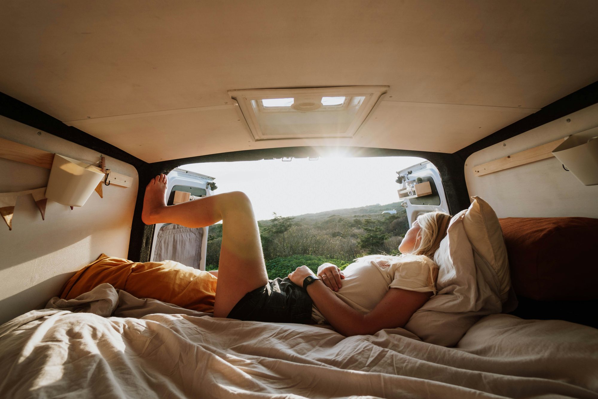 Mujer descansando en la cama de una camper con la puerta abierta al paisaje