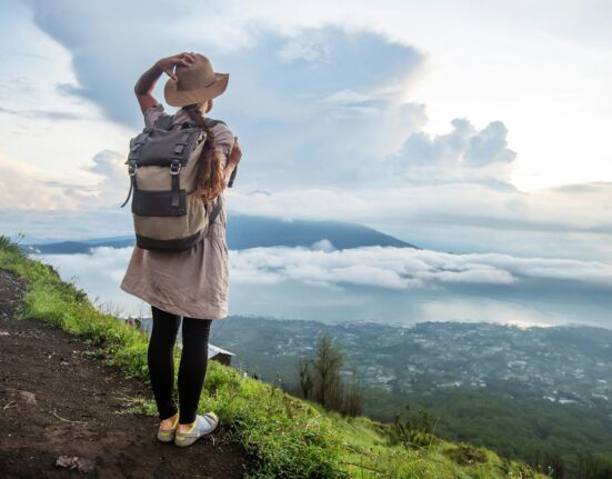 Viajera con mochila y sombrero mirando el valle desde un sendero