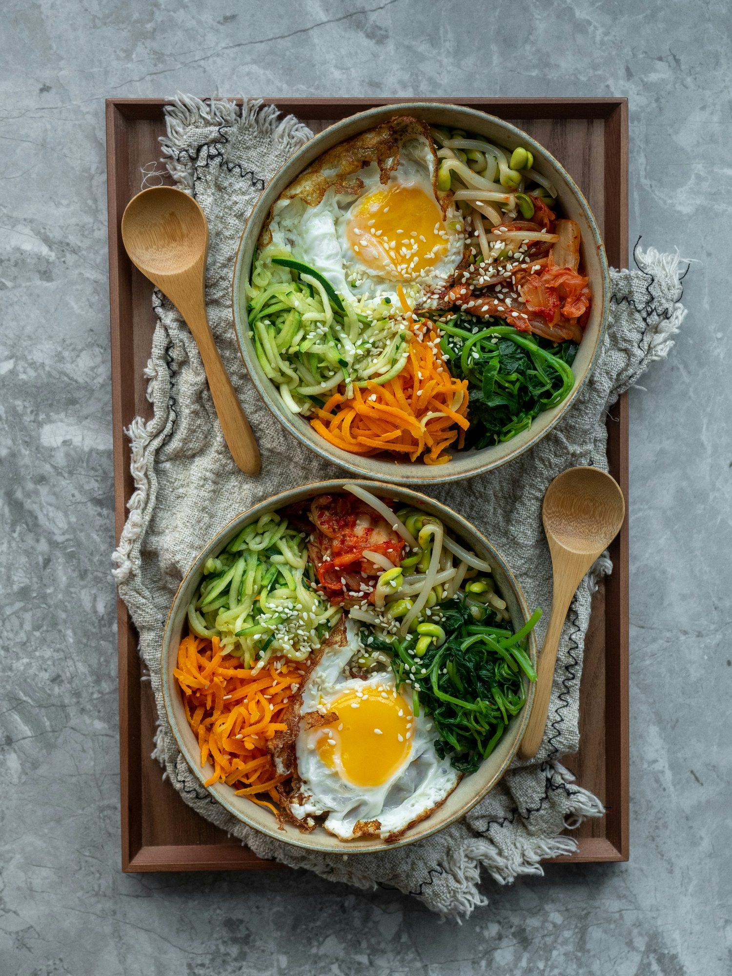 Dos bowls con huevo, verduras y arroz en una bandeja de madera